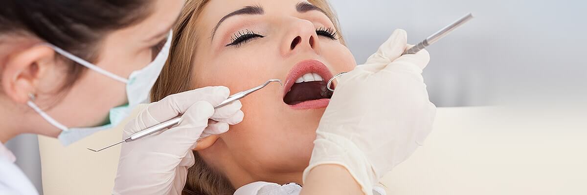 Sedated woman on exam chair as dentist examines her teeth